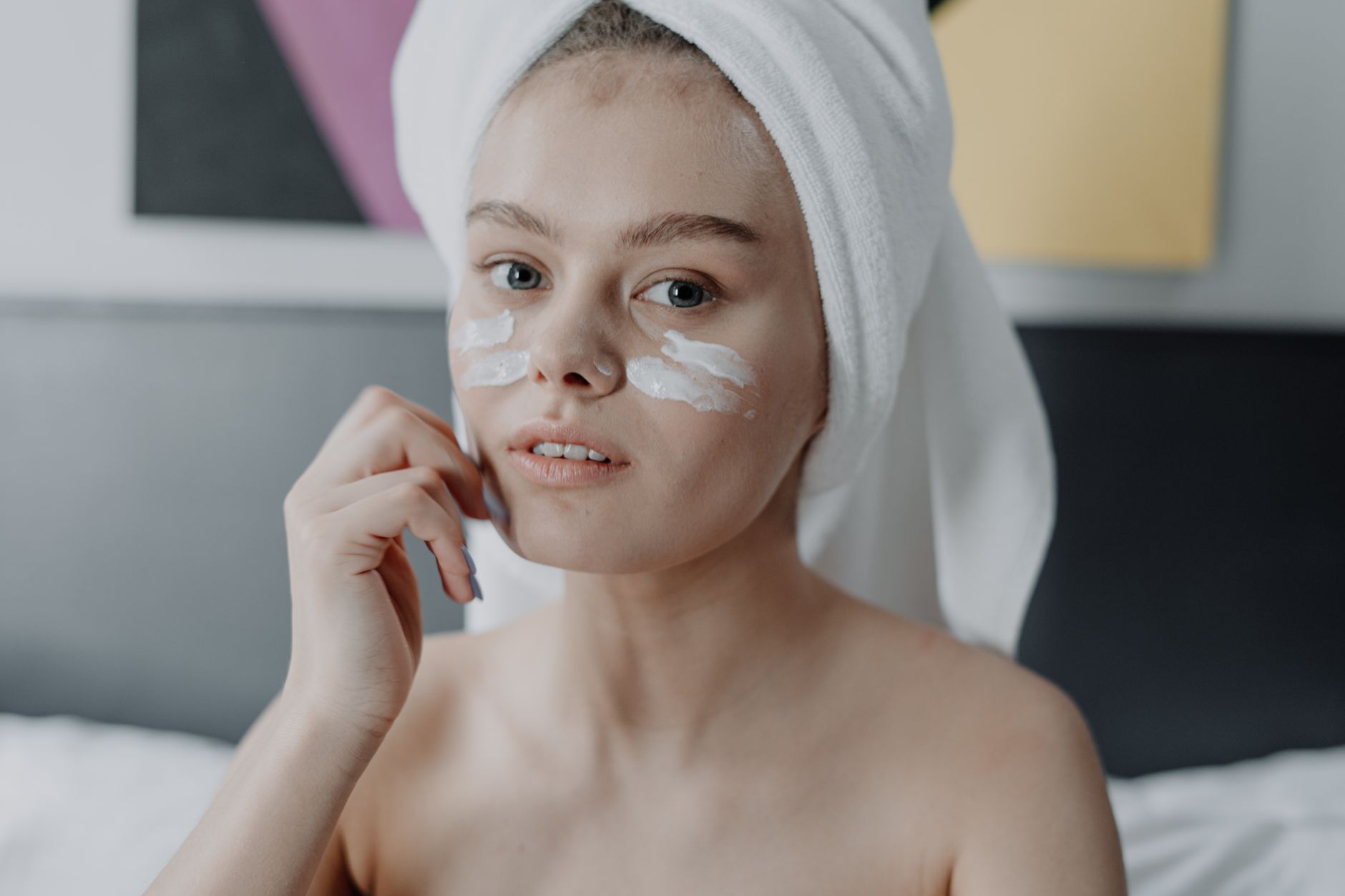 A young woman with facial cream and a towel wrapped on her head, focused on skincare.