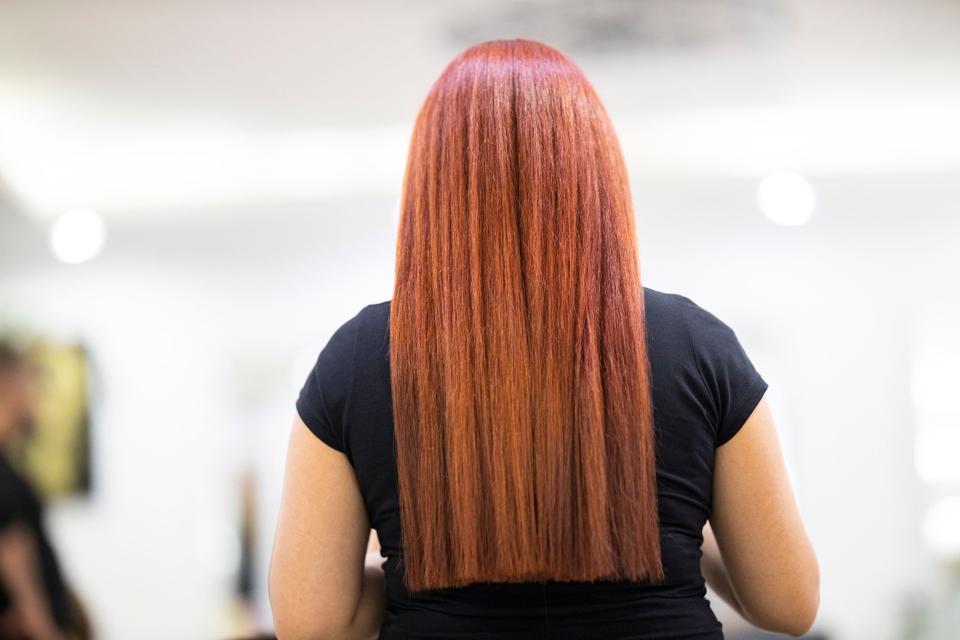 A woman with straight, vibrant red hair seen from the back, showcasing a fresh hairstyle in a professional salon.