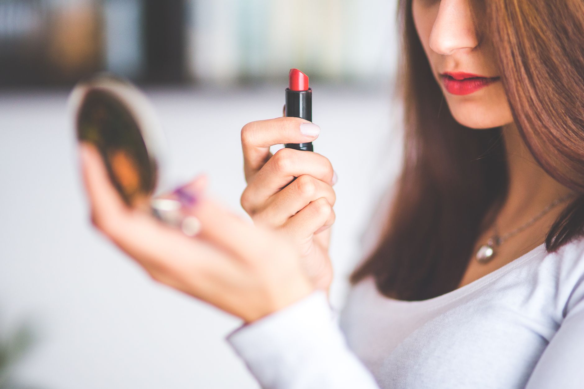 Close-up of woman applying red lipstick while holding a compact mirror.