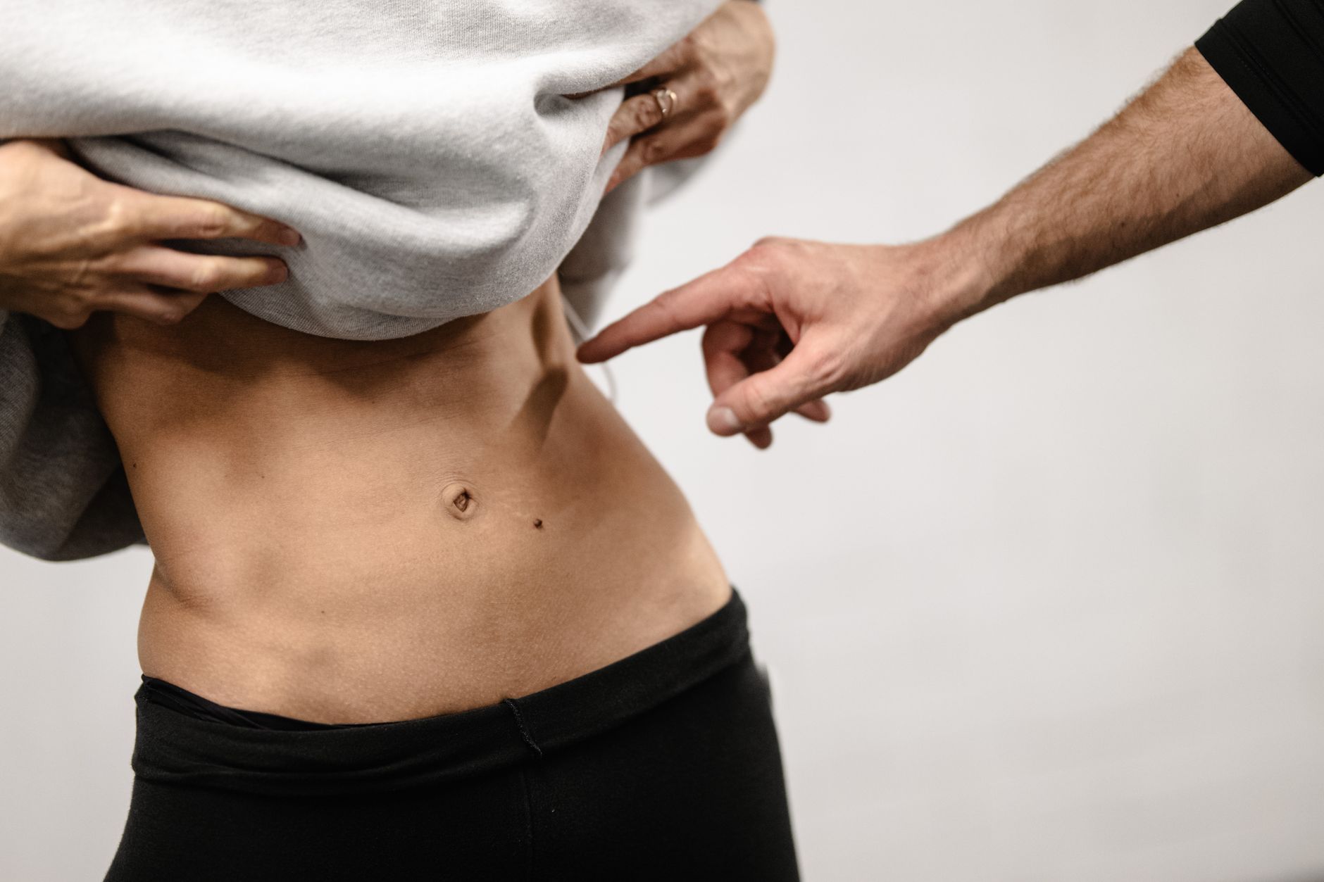An intimate close-up of a person's toned abdominal area with a hand pointing, emphasizing fitness.